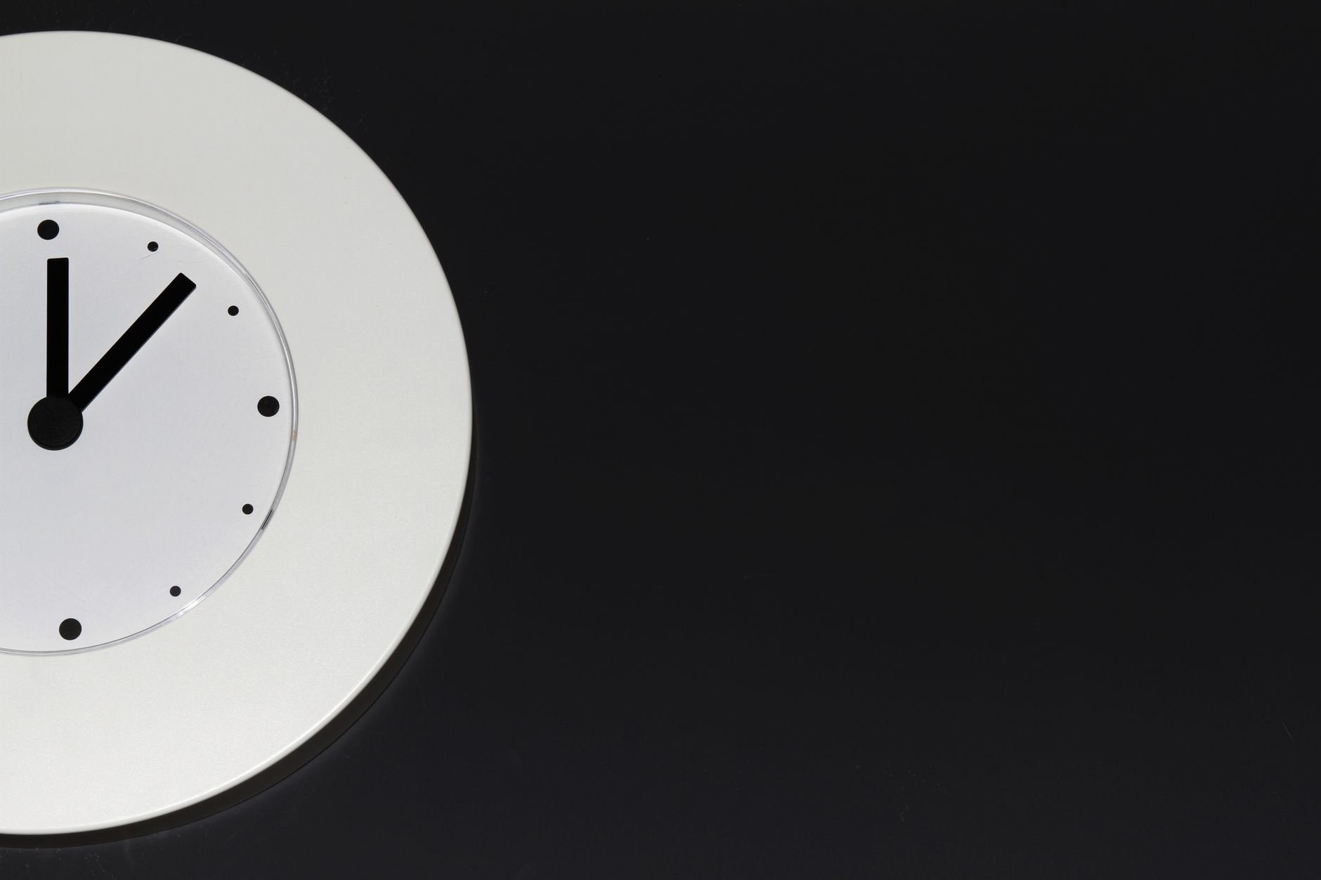 A plain white wall clock with black hands against a grey wall