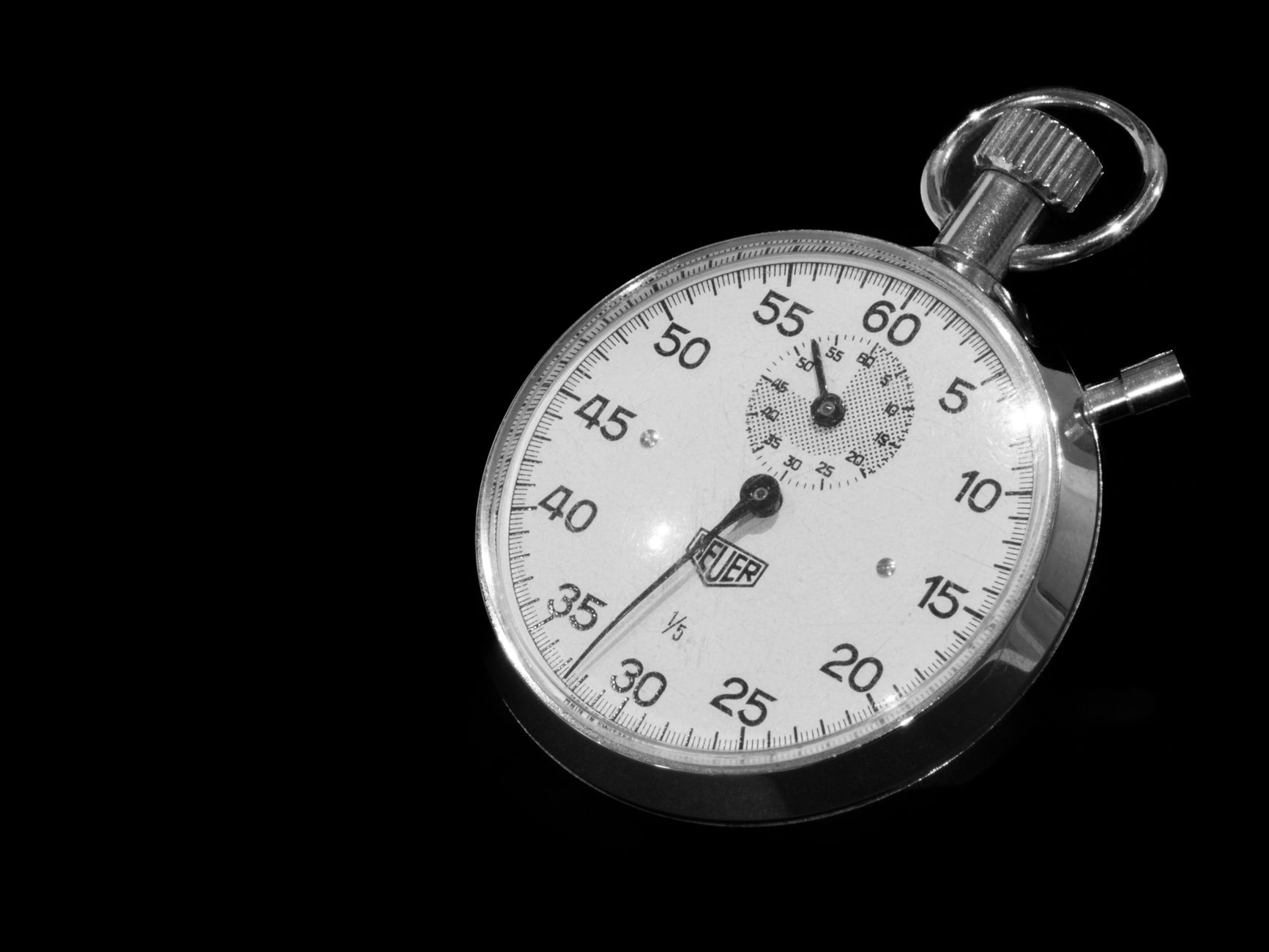 A silver stopwatch on a dark surface with its hands near the top